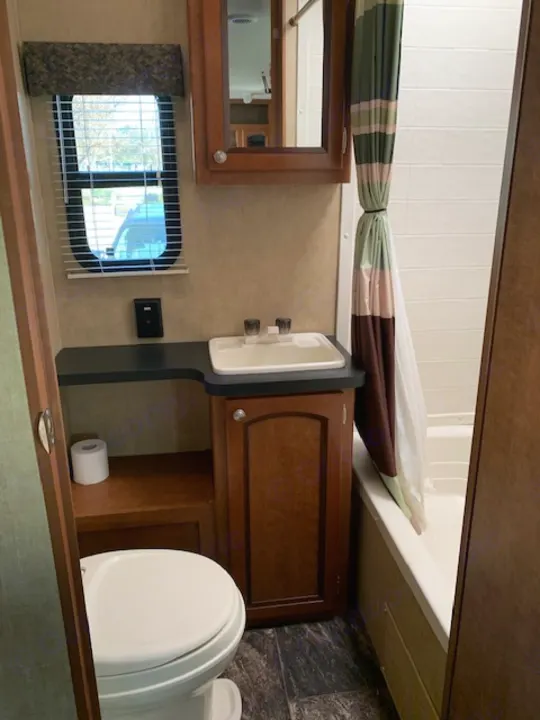 View inside an RV rental bathroom: a white toilet, sink, vanity, and a neatly tied-back striped shower curtain.. Shasta Revere 2012