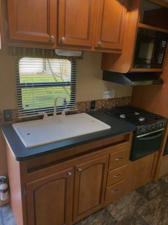 RV rental kitchen featuring wood cabinets, microwave, stove, and double sink, ready for travel meals.. Shasta Revere 2012
