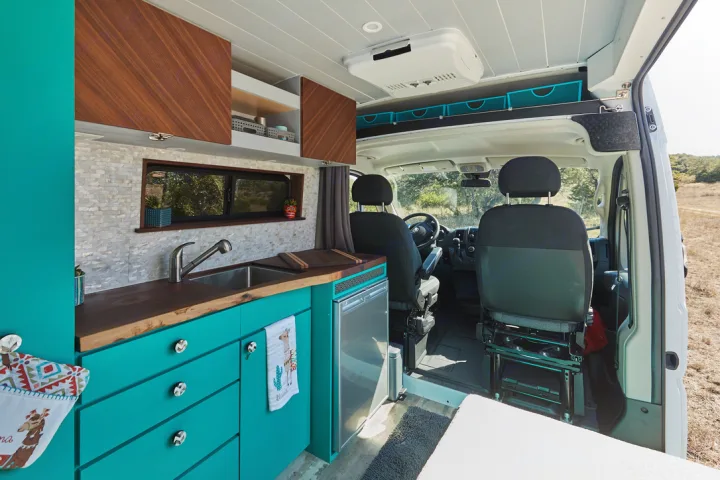 Step into this colorful RV rental's interior! Features a vibrant teal kitchen, wood countertops, and modern amenities for your road trip.. Dodge 2500 Promaster 2019