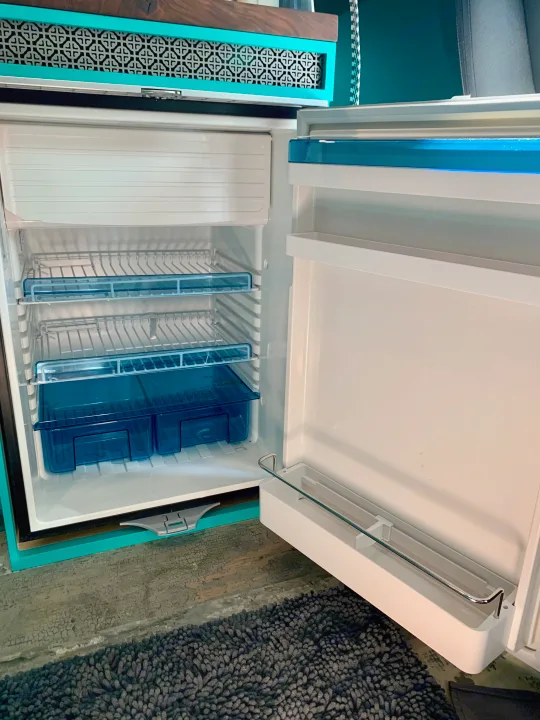 This empty, clean RV rental fridge offers ample storage with blue drawers, framed by stylish teal and wood.. Dodge 2500 Promaster 2019