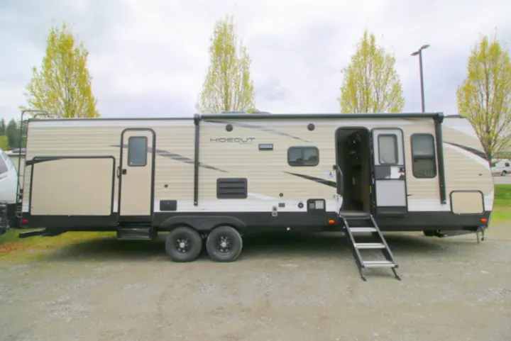 A spacious beige travel trailer, an ideal RV rental, is shown with steps extended from its open door on gravel.. Keystone Hideout 2020