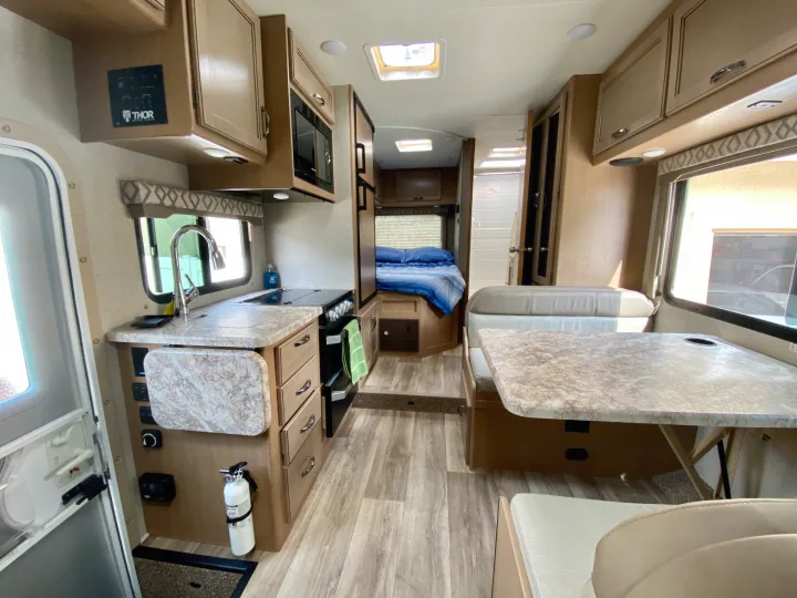 Inside a clean rv rental: kitchen with stove & sink, dinette, bed, and bathroom door visible.. Thor Motor Coach Four Winds 2020