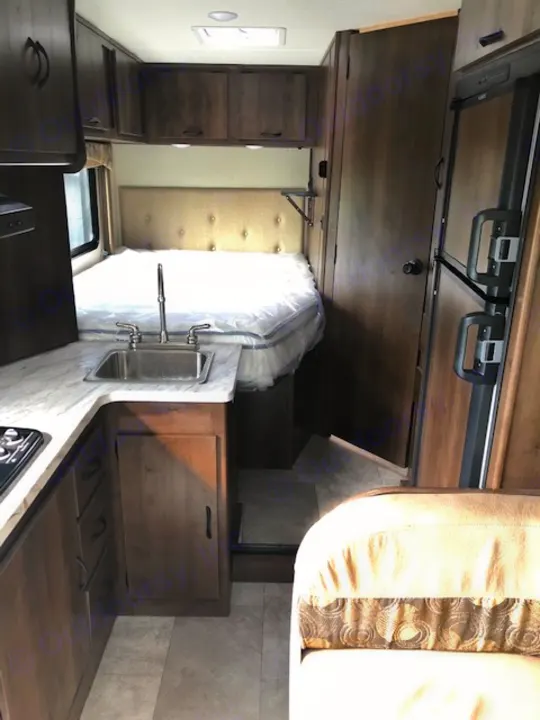 RV rental interior: a bedroom with new, plastic-wrapped mattress opposite a compact kitchen with a sink.. Ford Freelander 20CB 2018