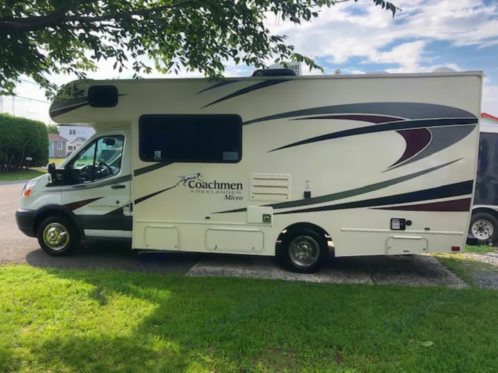 Side view of a light-colored Coachmen Freelander Micro RV rental, parked outdoors on a sunny day with green grass. Explore!. Ford Freelander 20CB 2018