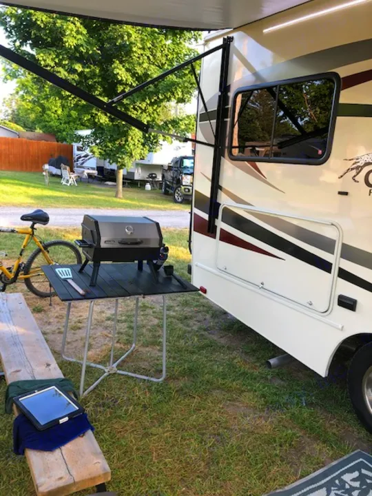 RV rental at a campsite. Awning, grill, bike, and tablet setup for outdoor relaxation.. Ford Freelander 20CB 2018