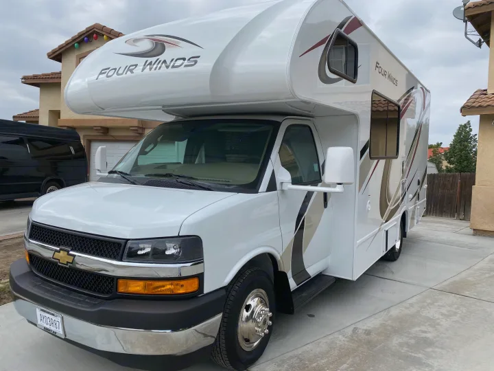 White Four Winds motorhome, an ideal RV rental, parked on a concrete driveway. Features brown and black accents.. Thor Motor Coach Four Winds 2020
