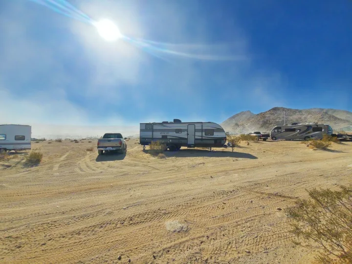 RV rental in the sunny desert: a bright day at a dry camping spot with travel trailers, motorhomes, and trucks on sand.. Forest River EVO 2020