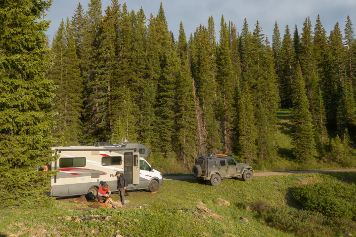 RV rental adventure: A camper and Jeep parked in a serene forest, with people by a fire pit enjoying dispersed camping.. Winnebago View 2017