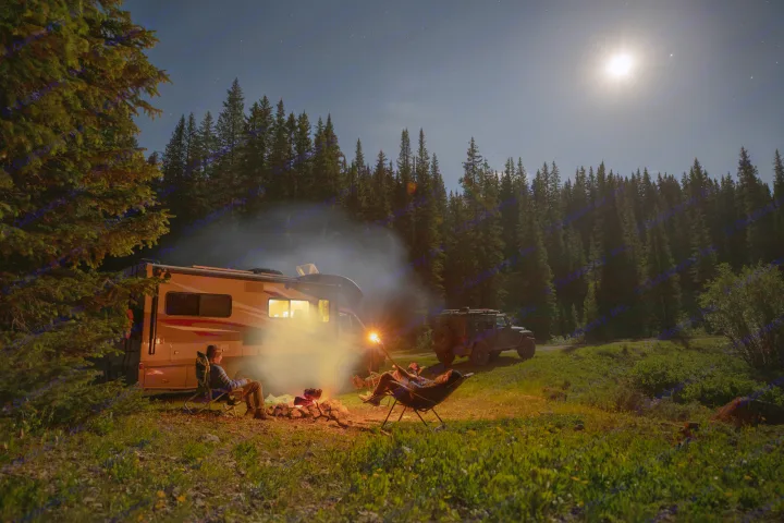Enjoying a serene night camping under the stars by an RV rental campfire with friends in a forest clearing.. Winnebago View 2017