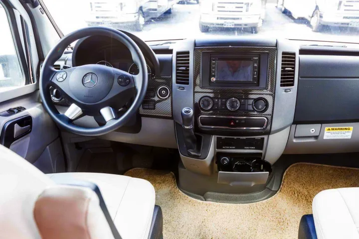 Modern RV rental interior: Mercedes-Benz Sprinter dashboard, steering wheel, multimedia screen, and driver's cabin controls.. Winnebago View 2017