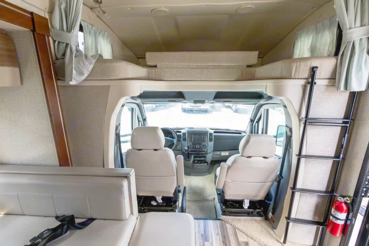Interior of an RV rental showing the cockpit, an overhead bunk bed with a ladder, and a living area.. Winnebago View 2017