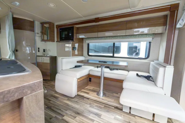 Modern RV rental interior: cozy dinette with white cushions, kitchen, and wood-look floor for comfortable travel.. Winnebago View 2017