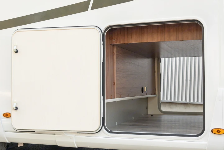 Accessing storage on an RV rental: large exterior compartment open, revealing a wood-paneled interior and floor.. Pilote P746 A 2025