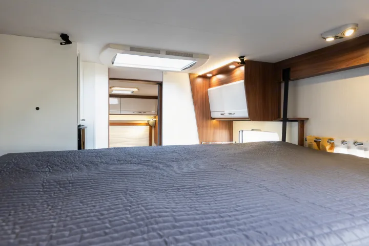 RV rental: A cozy bedroom with a grey quilted bed, leading to a compact living and kitchen area.. Pilote P746 A 2025