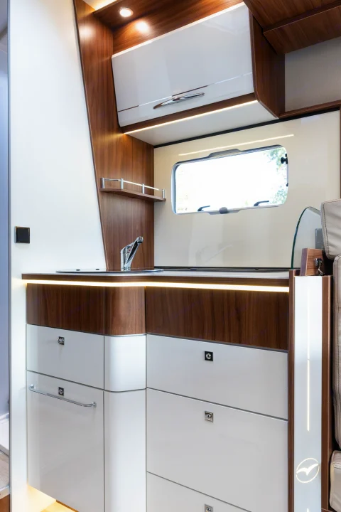 Modern rv rental galley featuring sleek wood and white cabinetry, a sink, and integrated lighting for comfortable travels.. Pilote P746 A 2025