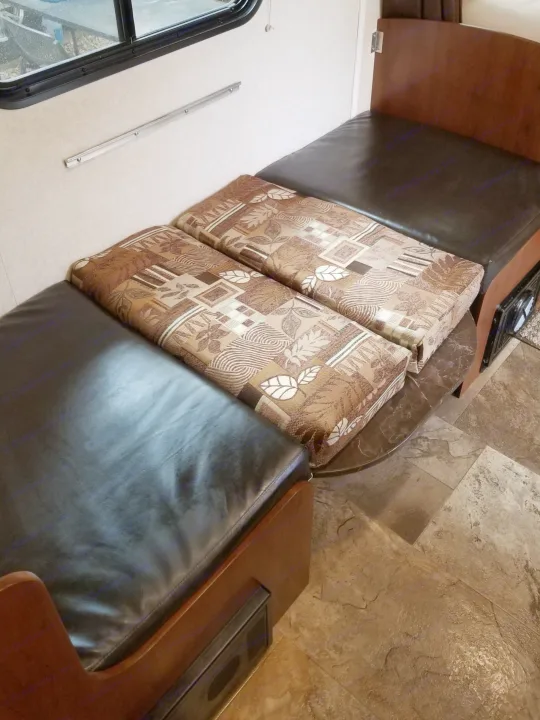 RV rental dinette shows black benches and patterned cushions, ideal for seating or a convertible bed.. Jayco SLX - 21.5' 2017