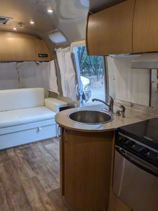 Clean rv rental interior with kitchen, sink, stove, white sofa, and wood floor. Ideal for travel.. Airstream Safari 2008