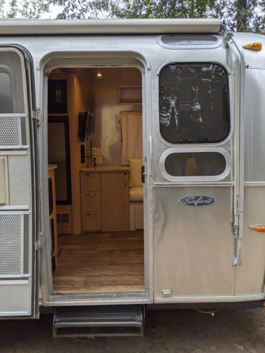 Step inside this Airstream Safari RV rental. The open door reveals a cozy travel trailer interior with wood floors and seating.. Airstream Safari 2008