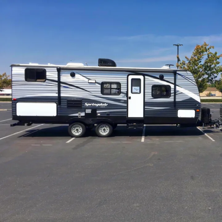 Side view of a silver and black "Springdale" travel trailer RV rental, parked in an open paved lot on a sunny day.. Keystone Springdale 2017