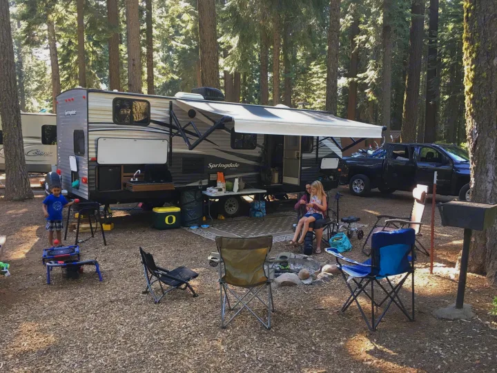 Family enjoying their RV rental at a shaded campground with campfire and outdoor kitchen setup.. Keystone Springdale 2017