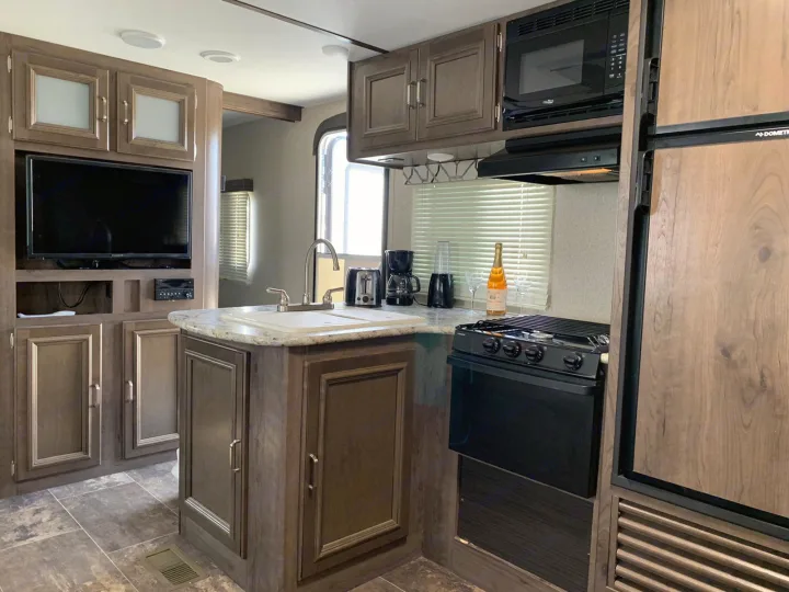 Spacious RV rental kitchen area features an island with sink, stove, microwave, fridge, TV, and small appliances.. Keystone Passport 2019