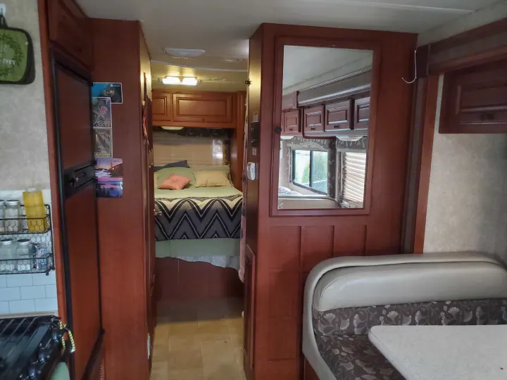 RV rental interior featuring a bedroom, kitchen with fridge, and a dinette area with booth seating.. Ford Fourwinds 2012