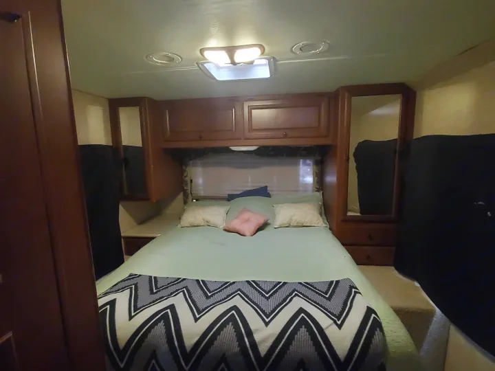 Cozy RV rental bedroom featuring a comfortable bed, overhead cabinets, and clever built-in storage. Ideal for travel.. Ford Fourwinds 2012
