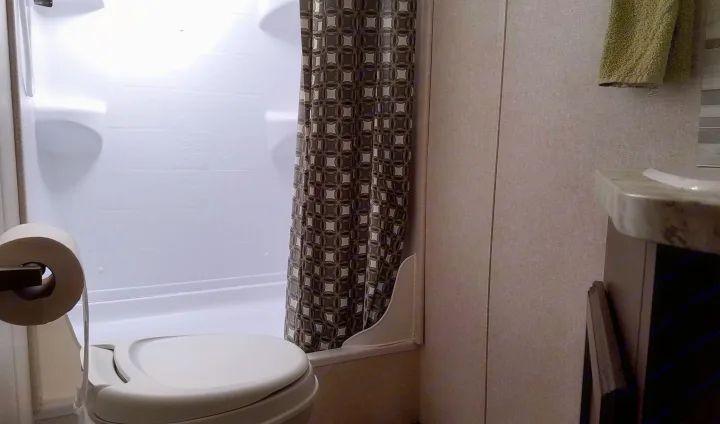 Inside an RV rental, a compact bathroom features a toilet, shower with a patterned curtain, and a partial view of a vanity.. Jayco Jay Flight SLX 2018
