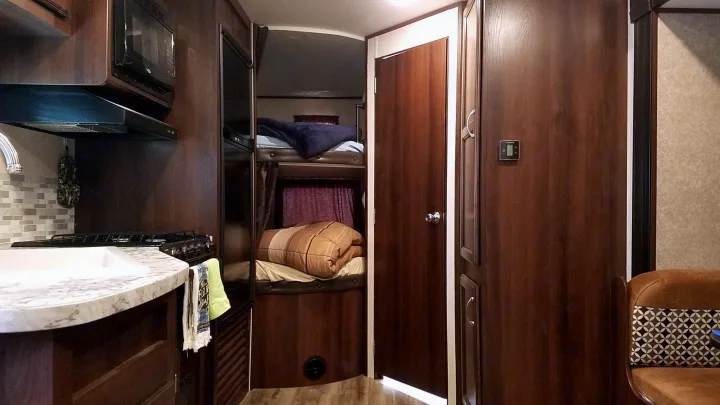 Cozy RV rental interior with compact kitchen, bunk beds, and warm wood finishes, perfect for family travel.. Jayco Jay Flight SLX 2018