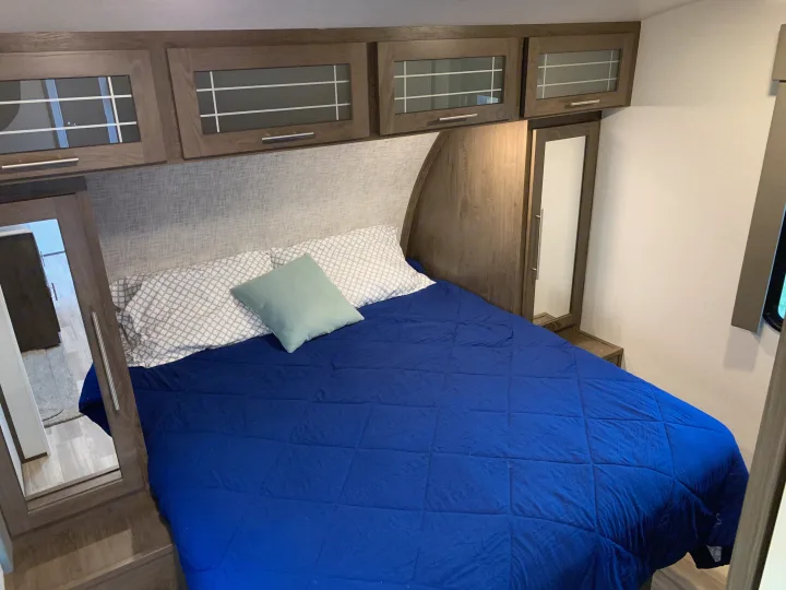 Comfortable RV rental bedroom with blue bed, overhead cabinets, and mirrored wardrobes.. Other Other 2019