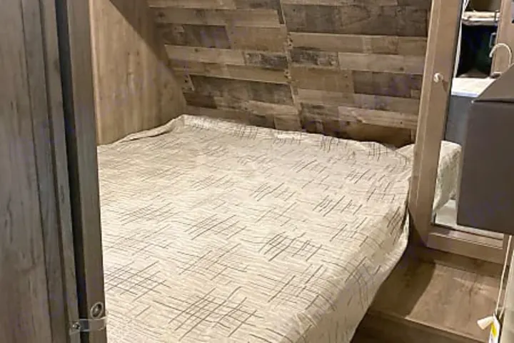 RV rental bedroom: a cozy bed with a light-colored duvet, surrounded by wood-paneled walls. A mirror is on the right.. Dutchmen Aspen Trail 2020
