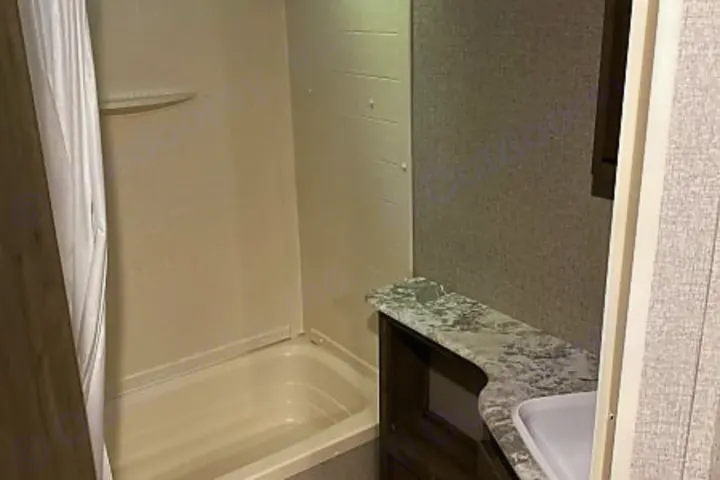Interior of an RV rental bathroom with a white shower/tub combo, vanity, and sink. Compact and functional for travels.. Dutchmen Aspen Trail 2020