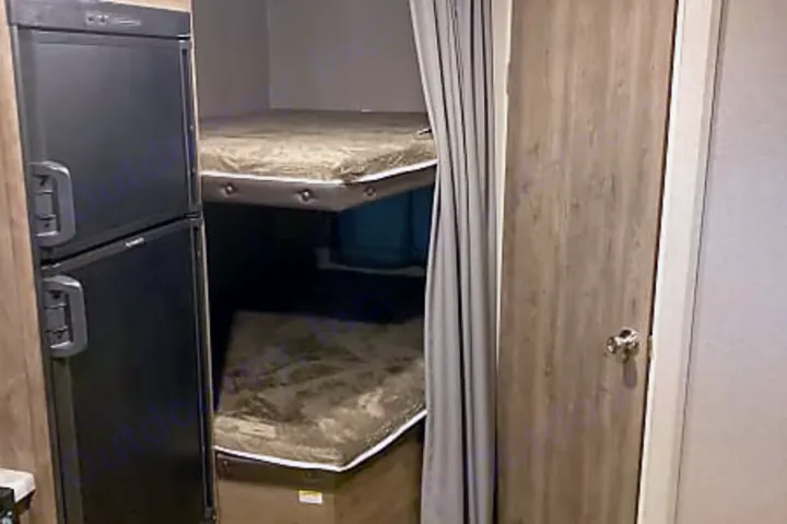 Cozy RV rental interior with bunk beds, a black refrigerator, and a privacy curtain. Perfect for family travel.. Dutchmen Aspen Trail 2020