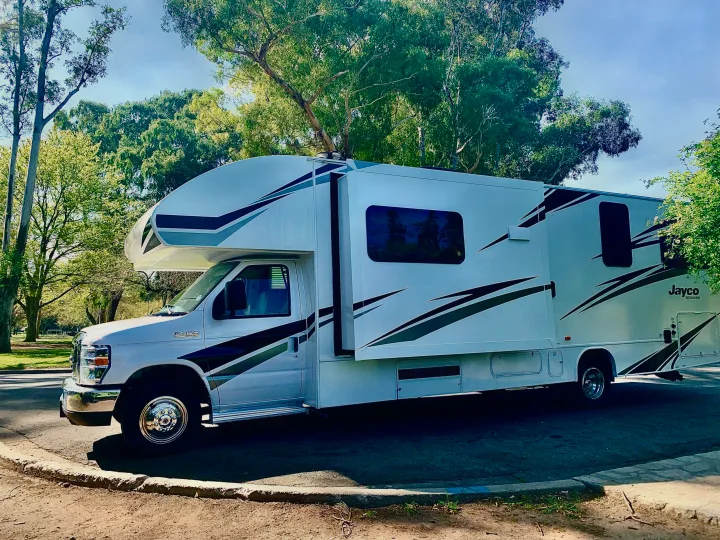 Bright white Class C Jayco Redhawk RV rental parked in a sunny outdoor setting with lush trees, ready for adventure.. Jayco Redhawk 2019