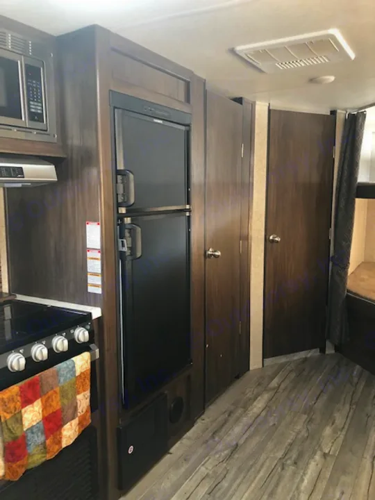 **RV rental** interior: a compact kitchen featuring a stove, microwave, and dark wood cabinets, perfect for travel.. Forest River Cherokee Grey Wolf 2019