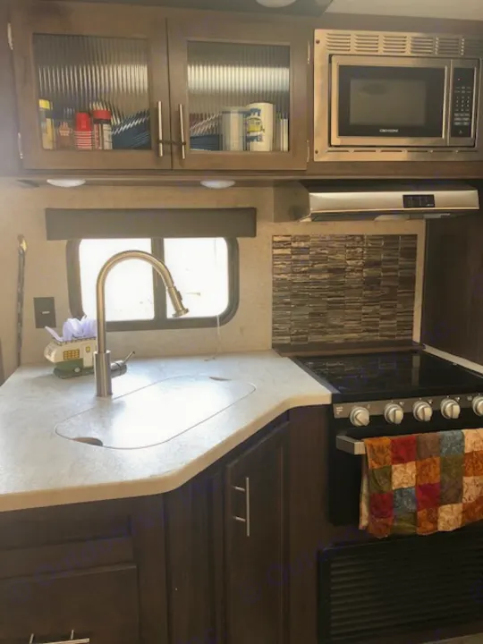 RV rental kitchen interior featuring a microwave, sink, stovetop, and organized cabinets. Ideal for travel adventures.. Forest River Cherokee Grey Wolf 2019