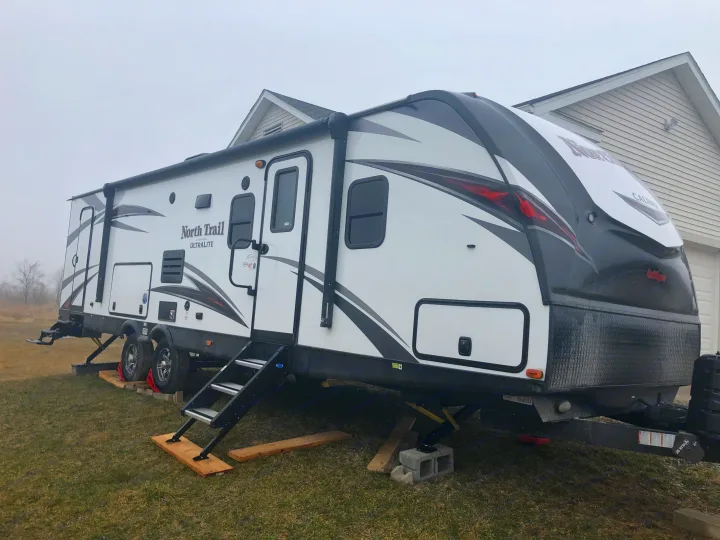 White North Trail travel trailer RV rental, stabilized on grass with steps down, parked near a house.. Heartland North Trail 2019