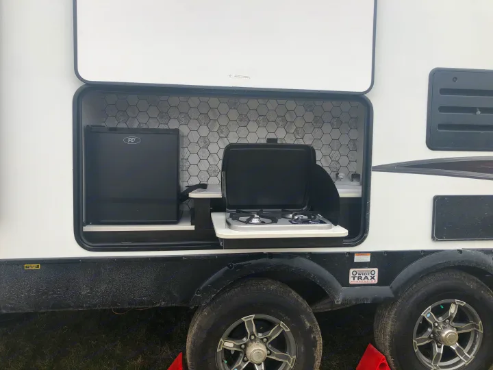 An RV rental with an outdoor kitchen setup: mini-fridge, 2-burner stove, and sink with a hexagonal backsplash.. Heartland North Trail 2019