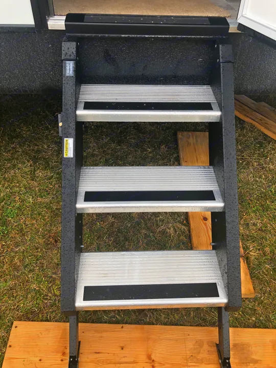 Wet RV rental steps on wood planks, providing temporary access to the vehicle from a grassy patch.. Heartland North Trail 2019