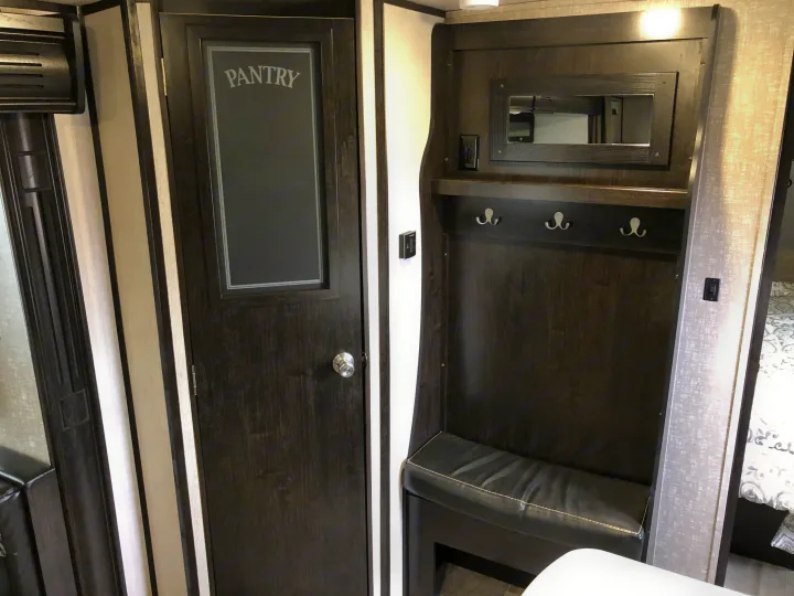 Compact RV rental interior: dark wood pantry, mirrored entryway with bench and hooks, plus power outlet.. Heartland North Trail 2019