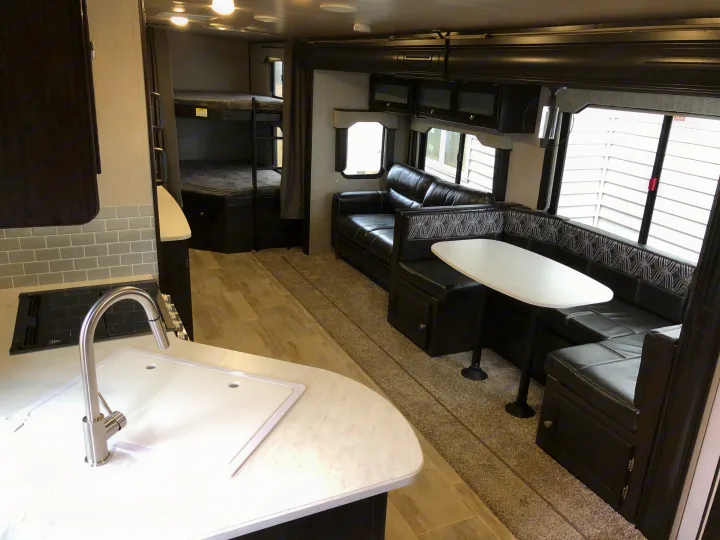 Spacious RV rental interior featuring a modern kitchen, bunk beds, and a comfy black leather dinette and sofa.. Heartland North Trail 2019