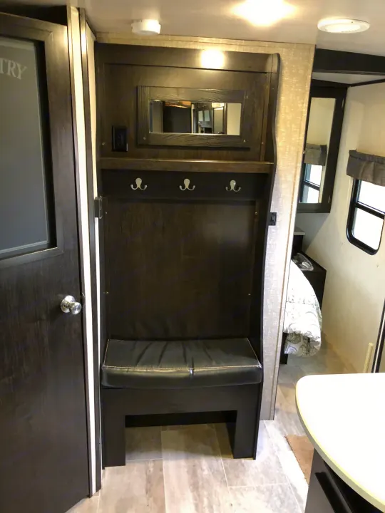 This compact RV rental features a dark wood built-in entryway: bench, hooks, and mirror. It leads to the bedroom area for organized living.. Heartland North Trail 2019