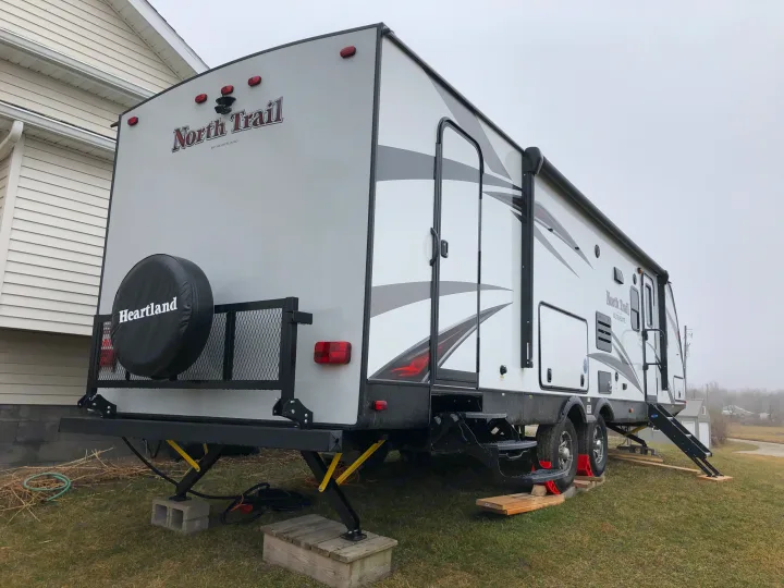 This North Trail Heartland RV rental is parked on grass, showing its leveled setup with jacks and extended steps.. Heartland North Trail 2019