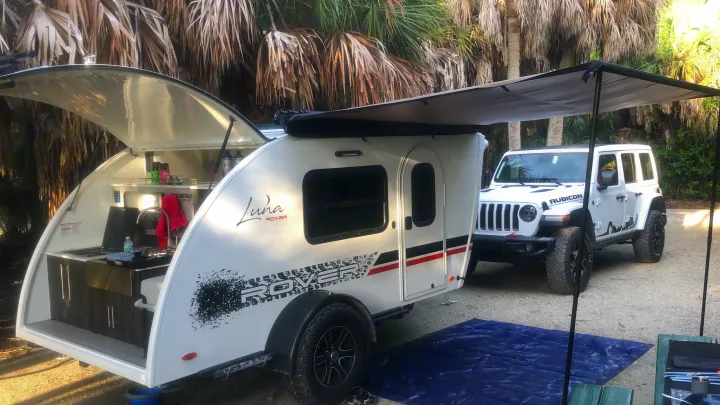 White Luna Rover teardrop RV rental with open galley kitchen & awning, paired with a white Jeep Rubicon.. InTech RV InTech RV Trailer 2021