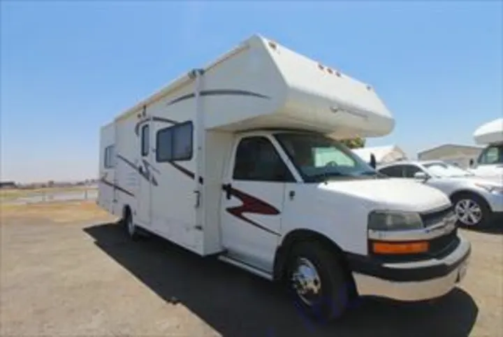 A bright white Class C RV rental, a large motorhome with a slide-out, parked on dirt under a clear sky, ready for adventure.. Forest River Sunseeker 2007