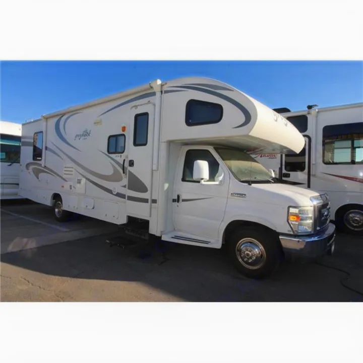 White Class C RV rental parked outdoors under a blue sky, featuring sleek gray graphics and an extended awning.. Jayco Greyhawk 2017