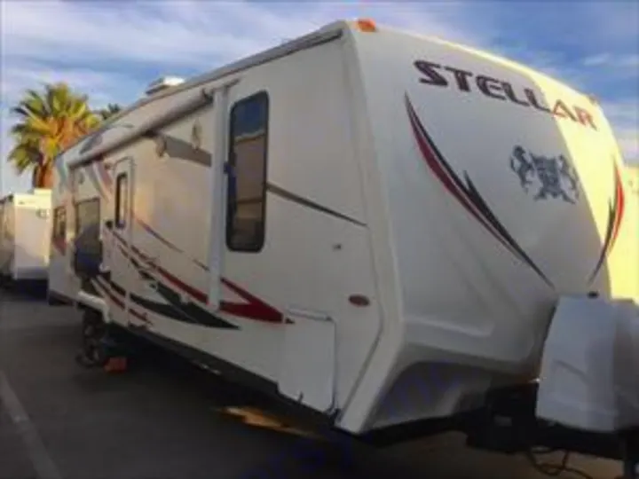This white Stellar toy hauler travel trailer with red & black graphics makes a perfect rv rental for adventures. Parked outdoors.. Eclipse Stellar 2013
