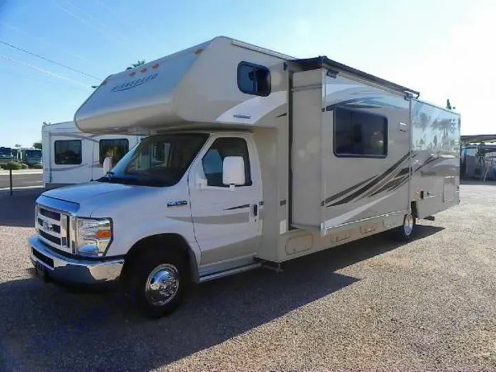 A tan and white Class C motorhome (RV) with an extended slide-out is parked on gravel. Great for RV rental trips.. Winnebago Minnie Winnie 2016