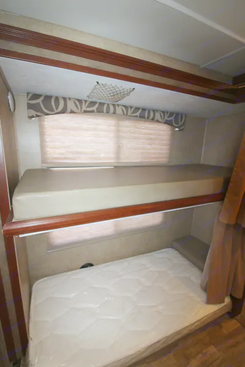 RV rental: Compact bunk beds with mattresses, window blinds, and storage net in this cozy camper interior.. Forest River Forester 2016