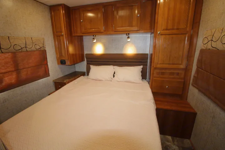 Well-appointed RV rental bedroom with bed, ample wood storage cabinets, and warm lighting. Ideal for travel.. Coachmen Leprechaun 2018